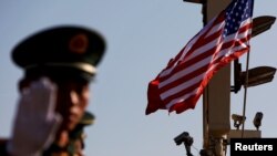 FILE - A paramilitary policeman gestures under a pole with security cameras and U.S. and Chinese flags near the Forbidden City ahead of a visit by U.S. President Donald Trump to Beijing, Nov. 8, 2017. 