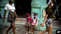Wearing masks as a precaution against the spread of the new coronavirus Angelica Victoria, center left, and Thalia Oneida, wait for their parents sitting on a chair in Havana, Cuba, Oct. 12, 2020. 