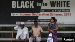 People wait in front of an income tax billboard at a bus stop in New Delhi, India, Sept. 26, 2016.