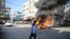 Um palestiniano celebra junto a um carro civil israelita em chamas retirado do kibutz de Kfra Azza em Beit Lahiya, Faixa de Gaza, sábado, 7 de outubro de 2023. Militantes do Hamas levaram a cabo um ataque sem precedentes, com várias frentes, contra Israel ao amanhecer de sábado
