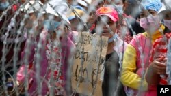 Cambodian garment workers shout slogans behind barbed wire set up by police near the Council of Ministers building during a rally in Phnom Penh, Cambodia, Monday, Dec. 30, 2013. The workers are demanding a raise in their monthly salary from US $160 to $80. (AP Photo/Heng Sinith)