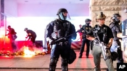 Law enforcement officers stand watch and extinguish a fire set by protesters behind the Mark O. Hatfield United States Courthouse in Portland.