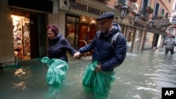 A couple wades their way through water in Venice, Italy, Nov. 15, 2019. (AP Photo/Luca Bruno)