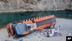 Locals gather supplies next to a damage bus at the site of accident in Khuzdar, a remote district in the Pakistan's southwestern Baluchistan province, June 11, 2021.