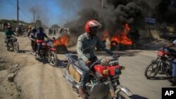 Demonstrators drive past a burning barricade set up by the police who are protesting bad police governance in Port-au-Prince, Haiti, Jan. 26, 2023.