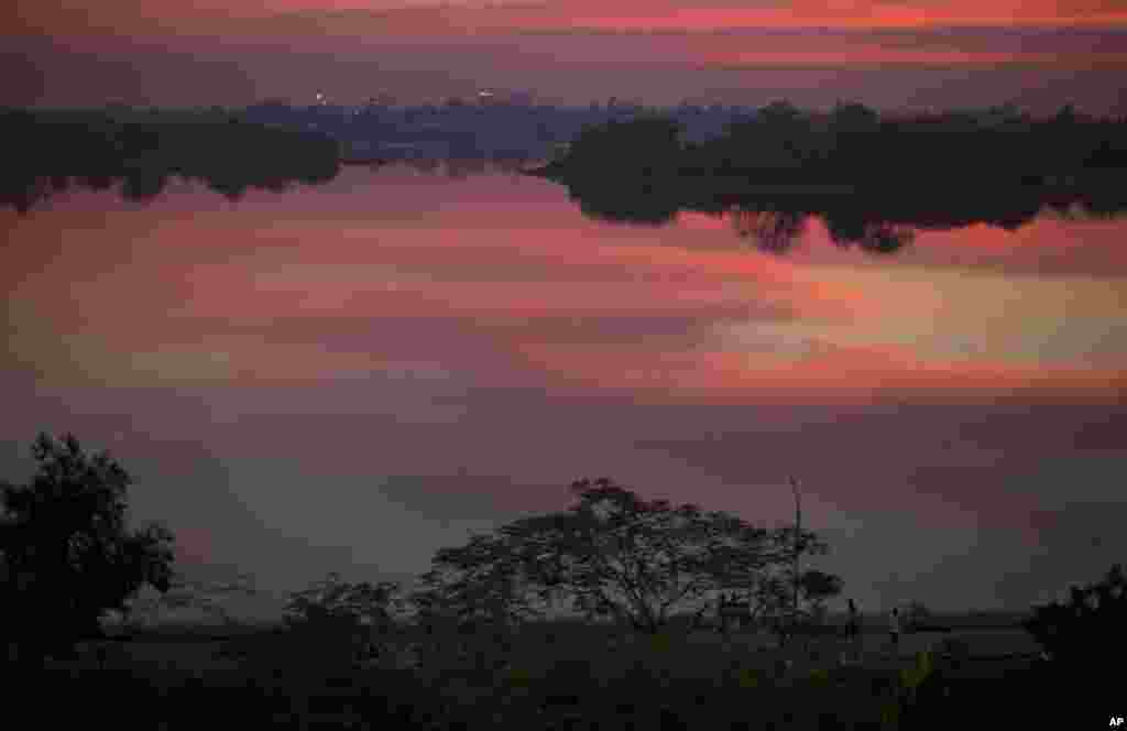 People walk on a path along a lake mirrored with clouds after sunset in Yangon, Myanmar.