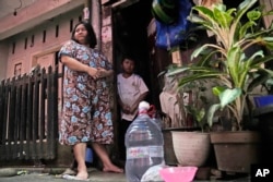 Devi Putri Eka Sari, a stay-at-home mother, stands outside her house with her son Satria Fareji, near bottles she uses to collect water, in Jakarta, Indonesia. (AP Photo/Dita Alangkara)