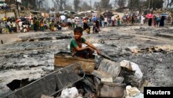 Seorang bocah pengungsi Rohingya duduk di atas tumpukan bahan yang terbakar setelah kebakaran besar terjadi dan menghancurkan ribuan tempat penampungan di kamp pengungsi Rohingya di Cox's Bazar, Bangladesh, 24 Maret 2021. (Foto: Reuters)