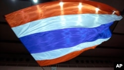 Seorang pendukung monarki Thailand mengibarkan bendera nasional raksasa di Bangkok, Thailand, 30 Agustus 2020. Pemerintah Thailand dan kelompok pemberontak utama menyepakati peta jalan terbaru yang bertujuan untuk membawa perdamaian di wilayah selatan itu. (Foto: AP)