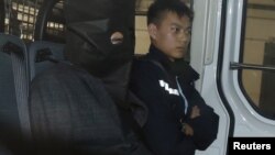 涉嫌在美国加州杀死自己两名侄子的石德云在香港被捕后坐在警车里，在警察旁边（2016年1月25日）