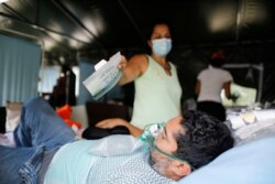 Una mujer muestra el empaque de una mascarilla a un paciente que padece COVID-19, mientras este recibe una máscara de oxígeno, en la carpa médica en el Poliedro de Caracas, el 21 de marzo de 2021.