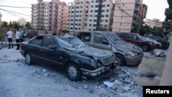 People stand near damaged vehicles at the site hit by an Israeli strike that, according to a security source, killed a Hamas leader, Saeed Atallah, and three family members, in the northern city of Tripoli, Lebanon, Oct. 5, 2024.