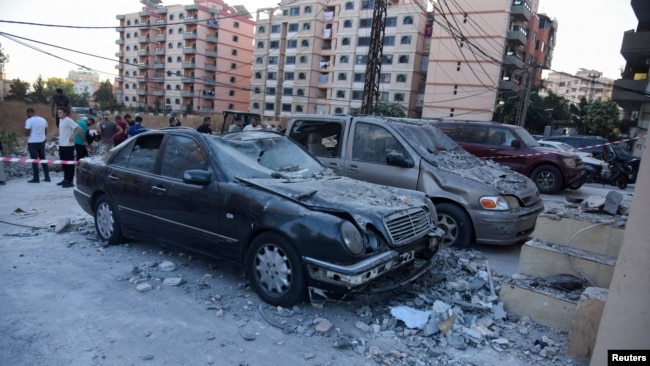 People stand near damaged vehicles at the site hit by an Israeli strike that, according to a security source, killed a Hamas leader, Saeed Atallah, and three family members, in the northern city of Tripoli, Lebanon, Oct. 5, 2024.