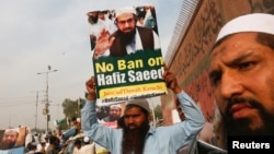 FILE - A supporter of Islamic charity organization Jamaat-ud-Dawa (JuD) carries a sign with others as they listen to the speech of leaders (unseen) to condemn the house arrest of Hafiz Saeed, chief of (JuD) during a protest demonstration in Karachi, Pakistan, Feb. 3, 2017. 