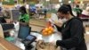 FILE - Yelitza Esteva, right, bags groceries for an order Wednesday, April 15, 2020, in Surfside, Fla. Esteva was a hairstylist. She now makes supermarket deliveries. 