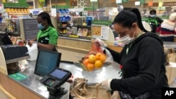 FILE - Yelitza Esteva, right, bags groceries for an order Wednesday, April 15, 2020, in Surfside, Fla. Esteva was a hairstylist. She now makes supermarket deliveries. 