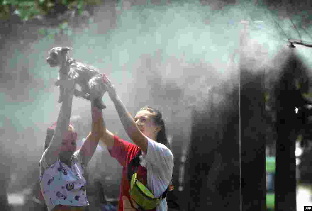 Girls refresh themselves and their dog with water spray frames set along the central street of the Ukrainian capital of Kyiv during a heatwave.