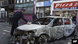 A police officer removes identification from a police car set on fire and burnt during riots in Tottenham, north London, August 7, 2011