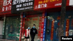 Personas con mascarillas caminan frente a tiendas cerradas debido al brote de coronavirus, en Jiujiang, China, el 4 de febrero de 2020.