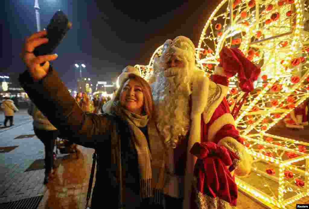 A woman poses for a picture with a participants dressed as Ayaz Ata (Father Frost) - the Kazakh equivalent of Santa Claus, during a procession through city streets marking the New Year and Christmas season in Almaty, Kazakhstan, December 25, 2023.&nbsp;