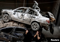 Para perempuan berdiri di samping kendaraan yang rusak di lokasi serangan udara Israel di Beirut, Lebanon, 11 Oktober 2024. (Foto: Louisa Gouliamaki/Reuters)