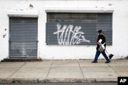 A person wearing a protective face mask as a precaution against the coronavirus walks past a shuttered business in Philadelphia, April 23, 2020.