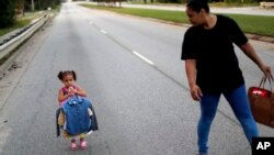 Rosemary Acevedo-Gonzalez (R) walks with her daughter Jordalis, 2, who asked to carry her own clothing after retrieving it upon returning to their home for the first time since it was flooded in the aftermath of Hurricane Florence in Spring Lake, N.C., Sept. 19, 2018.