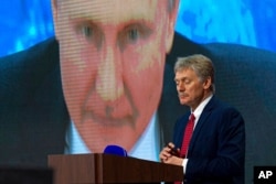 FILE - Russian President Vladimir Putin speaks via video call, as Kremlin spokesman Dmitry Peskov looks on, during a news conference in Moscow, Russia, Dec. 17, 2020.