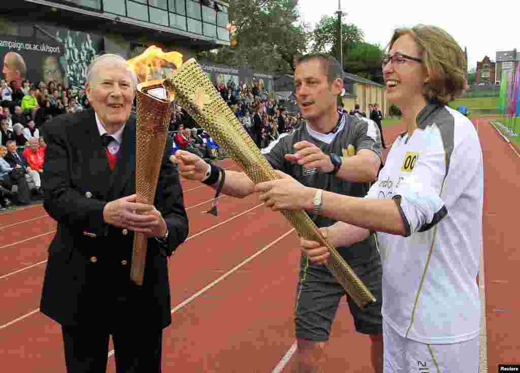 Roger Bannister (L) passes the Olympic flame to torchbearer Nicola Byrom during the London 2012 Olympic Games torch relay at the Iffley Road Stadium in Oxford, southern England July 10, 2012.