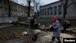 在饱受俄罗斯炮击的巴赫穆特，73岁的彼拉赫娅·米哈伊利夫娜(Pilaheia Mykhailivna)把她和邻居砍下的市区树木的枝干装上独轮推车，准备烧柴取暖。(2022年12月26日)