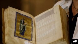 FILE - A Greek conservator holds up a repatriated 12th Century illuminated manuscript bible, during its presentation at the Byzantine Museum in Athens, Sept. 15, 2014.