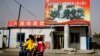 FILE - A Uyghur woman fetches schoolchildren as they ride past a picture showing China's President Xi Jinping joining hands with a group of Uyghur elders at the Unity New Village in Hotan, in western China's Xinjiang region, Sept. 20, 2018.