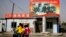 FILE - A Uyghur woman fetches schoolchildren as they ride past a picture showing China's President Xi Jinping joining hands with a group of Uyghur elders at the Unity New Village in Hotan, in western China's Xinjiang region, Sept. 20, 2018.