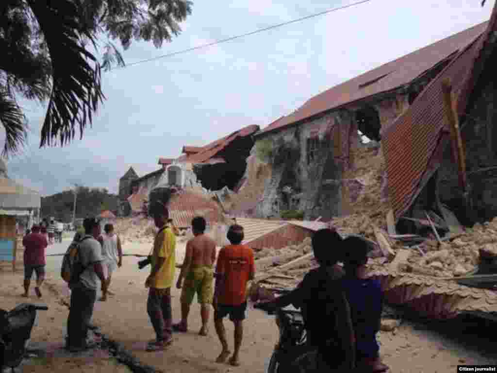 Warga berjalan dekat gereja yang hancur akibat gempa di Loboc, provinsi Bohol, Filipina (15/10). (Foto: Robert Michael Poole)