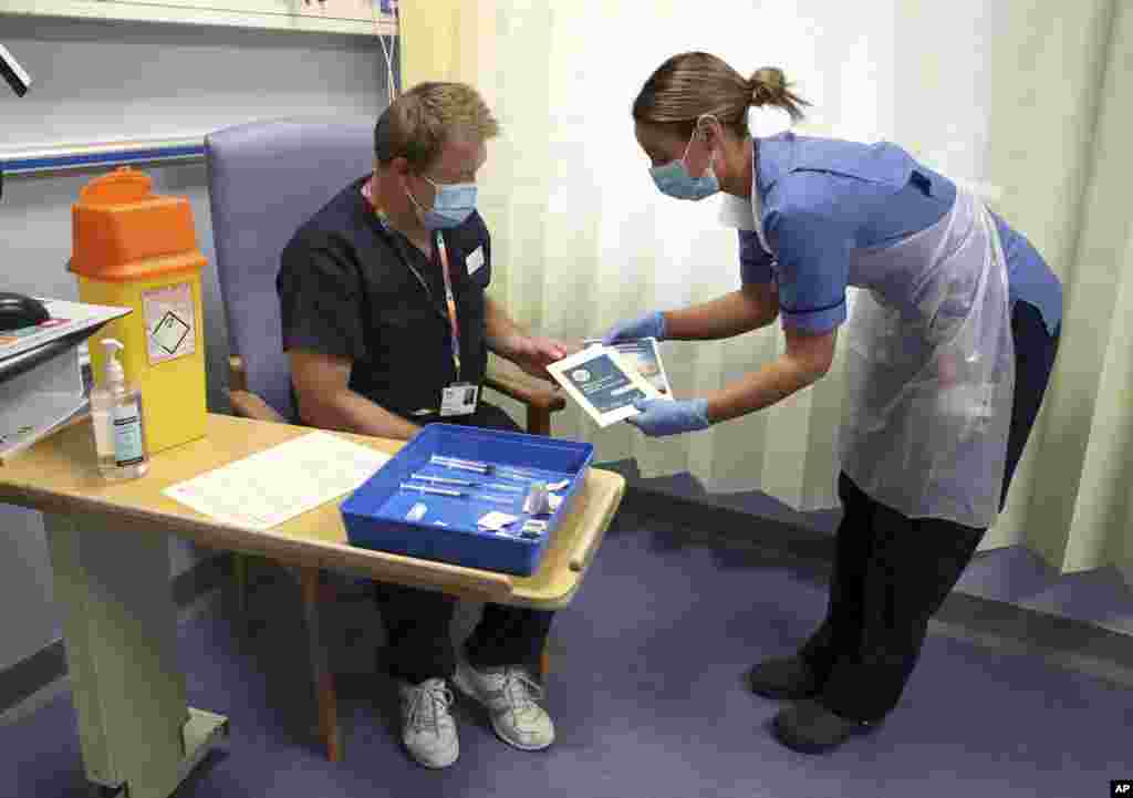 Deputy charge nurse Katie McIntosh show information about the Pfizer-BioNTech COVID-19 vaccine to Clinical Lead of Outpatient Theatres Andrew Mencnarowski at the Western General Hospital.