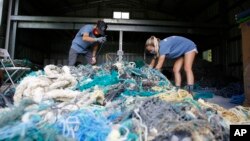 Hawaii Pacific University graduate student Drew McWhirter, left, and Raquel Corniuk, a research technician at the university's Center for Marine Debris Research, pull apart a massive entanglement of ghost nets on Wednesday, May 12, 2021 in Kaneohe, Hawaii. (AP Photo/Caleb Jones)