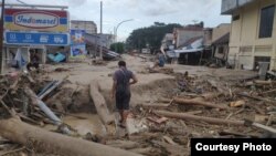 Seorang warga berjalan di antara batang-batang kayu yang terbawa air sungai yang meluap akibat banjir bandang di Luwu Utara, Sulawesi Selatan, 14 Juli 2020. (Foto: Tim SAR UNHAS Makassar)