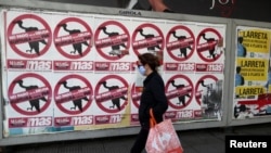 Seorang pejalan kali melewati poster yang bertuliskan "Jangan Bayarkan Utang. Keluar dari IMF" yang terpasang di jalanan kota Buenos Aires, Argentina, pada 27 Mei 2020. (Foto: Reuters/Agustin Marcarian)