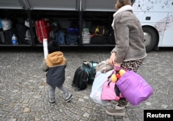 A mother and child stand in front of the possessions of Ukrainian refugees stowed in a coach to take them from a reception center in Munich to various accommodation facilities in Germany on Feb. 6, 2025. Some 7 million Ukrainians fled their country when Russia invaded.