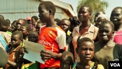 Refugees stand with a placard that reads: #ImmediateRelocation. Many refugees want to go to a settlement camp in Adjumani, but officials say these are full. ( Photo: Lizabeth Paulat for VOA)