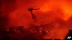 A helicopter drops water on the Cave Fire burning along Highway 154 in Los Padres National Forest, Calif., above Santa Barbara, Nov. 26, 2019. 