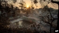 The sun rises behind a home leveled by the Holiday fire in Goleta, Calif., July 7, 2018. Evacuations were ordered as the fire edged into residential areas. 