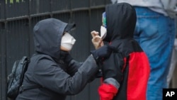 FILE - A woman adjusts her child's protective mask as they wait in line to be screened for COVID-19 at Gotham Health East New York, April 23, 2020, in the Brooklyn borough of New York City. 