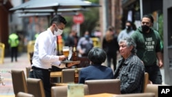 A waiter wearing a mask to curb the spread of the new coronavirus tends to a couple of customers outside a restaurant in the Usaquen neighborhood of Bogota, Colombia, Sept. 3, 2020. 