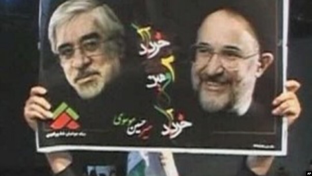 A protester holds up a poster of Iranian opposition leader Mir Hossein Mousavi (L) and reformist former president Mohammad Khatami during an anti-government rally in Tehran, 27 Dec 2009