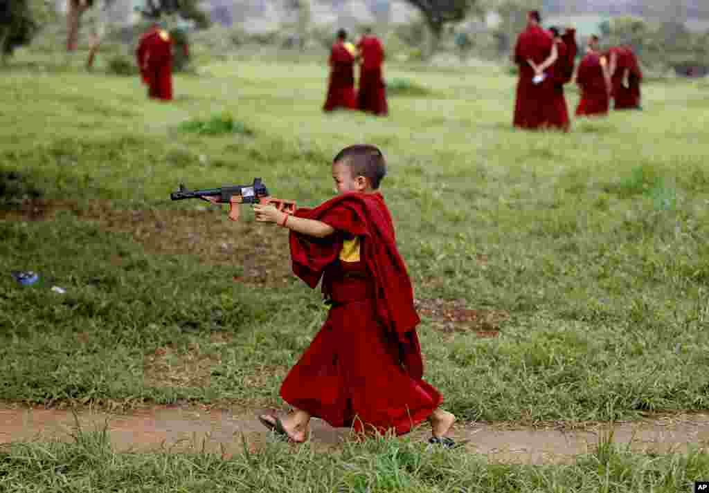 Seorang biksu muda Tibet bermain dengan pistol mainan saat istirahat dari khotbah keagamaan oleh pemimpin spiritual Tibet Dalai Lama, di luar Biara Tantra Gyudmed di Gurupura, India barat daya.