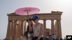 ARCHIVO - Turistas con un paraguas caminan frente al Partenón en la antigua Acrópolis en el centro de Atenas, 12 de junio de 2024. Junio ​​de 2024 fue el junio más caluroso registrado, según el servicio climático europeo Copérnico el lunes 8 de julio.