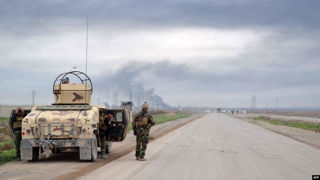 FILE - Smoke billows in the background as Kurdish peshmerga fighters take positions on the side of a road in the northern Iraqi city of Kirkuk, Jan. 30, 2015.