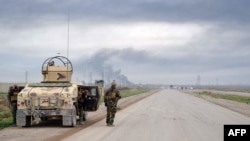 Tentara Peshmerga Kurdi tampak berjaga-jaga di pinggir jalan di wilayah Kirkuk, Irak utara, sementara di kejauhan tampak asap mengepul (30/1). 