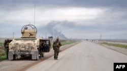 Smoke billows in the background as Kurdish Peshmerga fighters take positions on the side of a road in the northern Iraqi city of Kirkuk, Jan. 30, 2015.